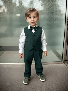 a young boy wearing a green suit and bow tie standing in front of a glass door