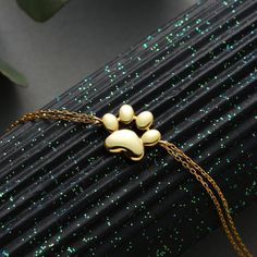 a gold dog paw charm on a black surface with green glitters and a plant in the background