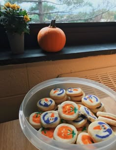 some cookies are sitting in a plastic container on a table near a pumpkin and window