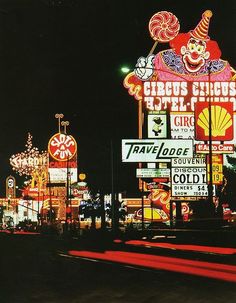 the neon signs are all lit up at night in front of an amusement park with clowns