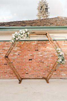 a wedding arch decorated with white flowers and greenery stands in front of a brick wall