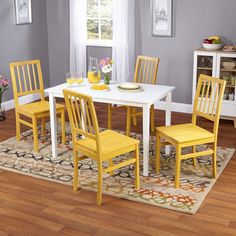 a dining room table with yellow chairs and a rug on the floor in front of it