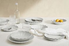 the table is set with white dishes and silver utensils, lemons, and wine bottles