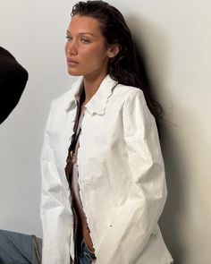 a woman leaning against a wall wearing a white shirt