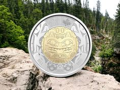 a gold and silver coin sitting on top of a rock in front of some trees