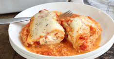 a white bowl filled with meat covered in sauce and cheese next to a silver fork