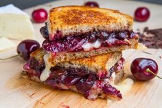 two grilled cheese sandwiches with cherries on a cutting board