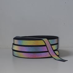 a rainbow colored ribbon on a white surface with a black strap around the neck and bottom