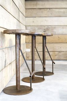 two metal stools sitting next to each other on top of a cement floor in front of a wooden wall