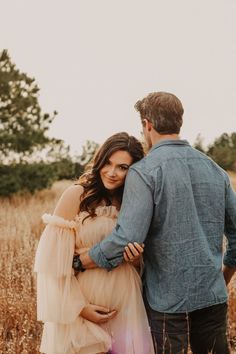 a pregnant woman standing next to a man in a field