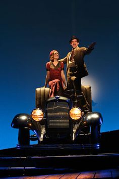 a man and woman standing on top of an old car in front of a blue sky