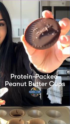 a woman holding up a chocolate peanut butter cupcake in front of some muffins