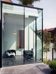 a glass walled room with a black chair and table in the center, next to a brick building