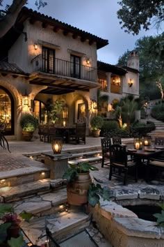 an outdoor dining area in front of a large house with candles lit up on the tables