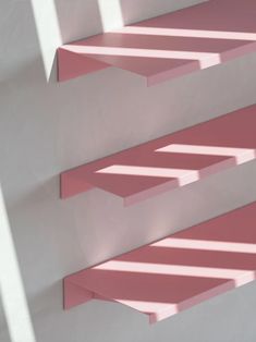 an abstract photo of pink and white shelves with shadows on the wall in front of them