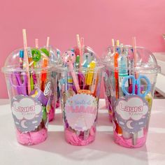 three cups with toothbrushes and pens in them on a table next to a pink wall