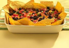 a white dish filled with black olives and guacamole, surrounded by tortilla chips