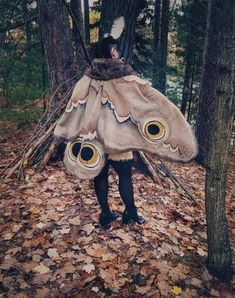 a woman is standing in the woods wearing a costume made out of leaves and feathers