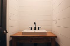 a bathroom sink sitting on top of a wooden counter next to a door with white shiping