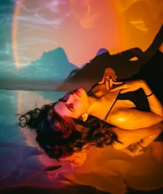 a woman laying on top of a bed under a rainbow colored sky