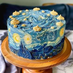 a blue cake with yellow icing and stars painted on the top is sitting on a wooden stand