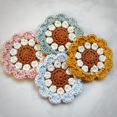 four crocheted flowers sitting on top of a white countertop next to each other