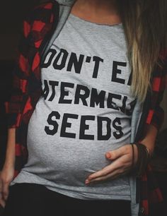 a pregnant woman holding her stomach while wearing a shirt that says don't e watermelon seeds