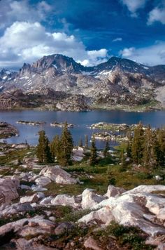 a lake surrounded by rocks and trees with mountains in the background