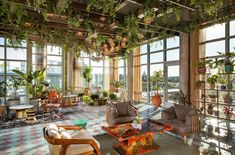 a living room filled with lots of furniture and plants hanging from the ceiling above it