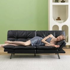 a woman laying on top of a black couch