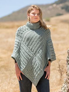 a woman standing in a field wearing a green knitted ponchy with an open neck