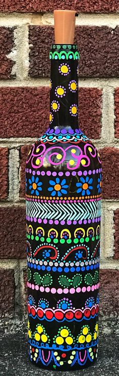 a colorful painted vase sitting on top of a table next to a brick wall with a potted plant in it