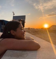 a woman laying on top of a sandy beach next to the ocean at sun set