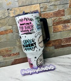 a travel mug with writing on it sitting next to a brick wall and sticker