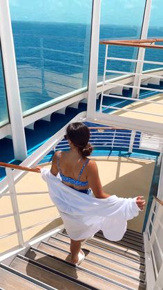 a woman in a white dress is walking up the stairs on a cruise ship looking out at the ocean