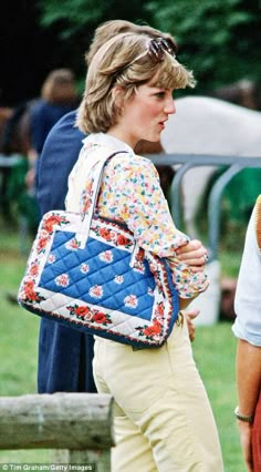 a woman carrying a blue quilted purse on her shoulder while walking in the grass