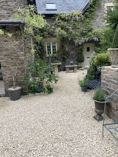 a stone house with potted plants and benches in the front yard, surrounded by gravel