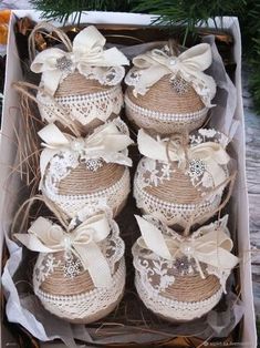 four baby booties in a box with white lace and bows on the top, sitting next to pine branches