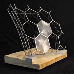 a metal sculpture sitting on top of a wooden block in front of a black background