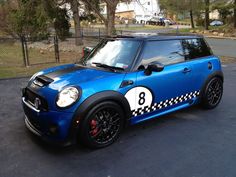 a blue mini with black and white stripes parked in a parking lot next to a fence