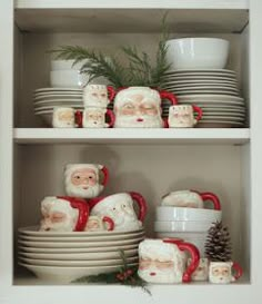 santa clause figurines on shelves with dishes and pine cones in the foreground