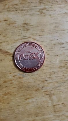 a close up of a wooden table with a coin on top of it and the word coca - cola written in red