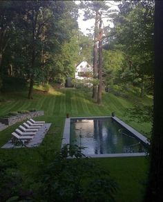 an empty pool in the middle of a lush green yard with lounge chairs around it