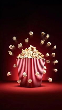 a red and white striped popcorn bucket filled with popcorn kernels on a black background