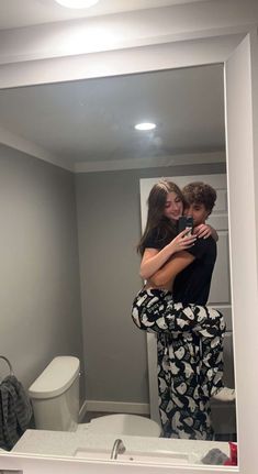 a man and woman hugging in front of a bathroom mirror