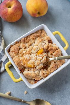 an apple crisp in a yellow dish next to two peaches on a blue surface