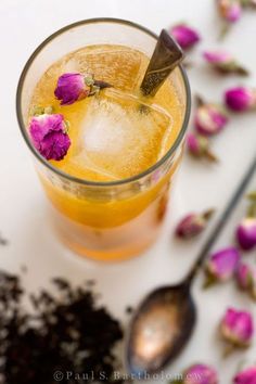 a glass filled with ice and flowers on top of a white table next to spoons