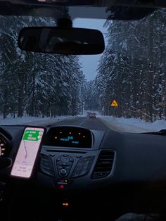 the dashboard of a car on a snowy road with trees in the backgroud