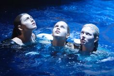 three people are swimming in a pool with blue water and one is looking up at the sky