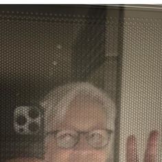 an older woman wearing glasses is looking out the window with her hand in front of her face